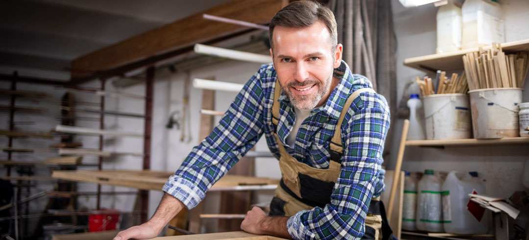 Hombre carpintero apoyando en una mesa y sonriendo