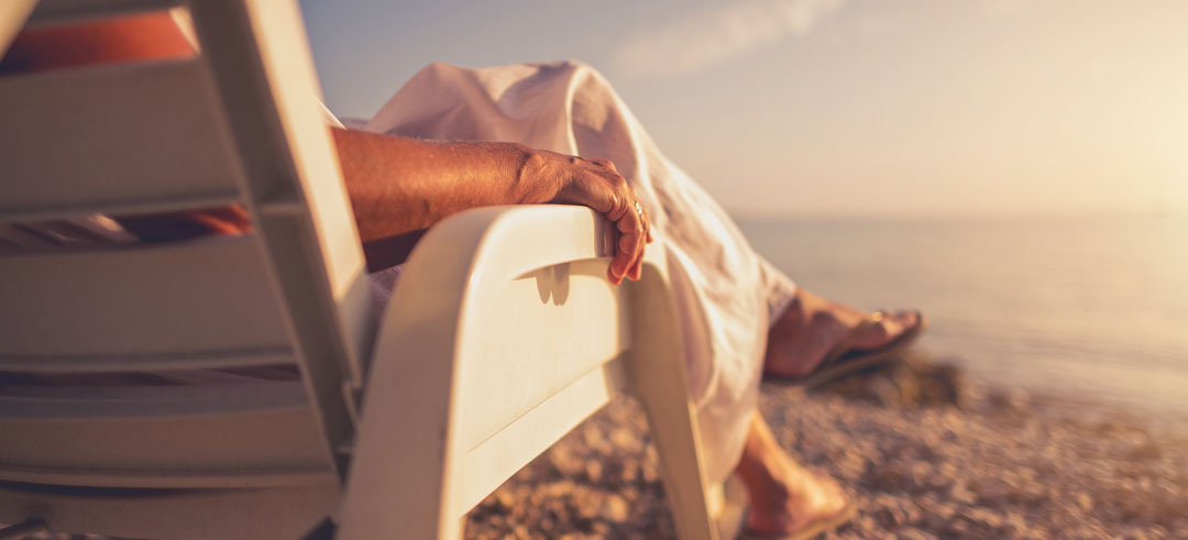 Persona tomando el sol y viendo el atardecer sentada en una silla en la playa