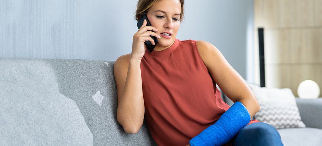 Mujer sentada en el sofá hablando por teléfono con el otro brazo escayolado